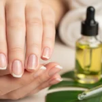 Zadbane dłonie z manicurem typu french oraz buteleczka olejku do skórek i pipeta na liściu jako element pielęgnacji.
