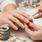 Zabieg manicure'u japońskiego – stylistka nakłada odżywczą pastę na paznokieć klientki przy pomocy pędzelka.