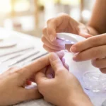 Stylistka utwardza przezroczysty tips na paznokciu klientki za pomocą mini lampy LED.