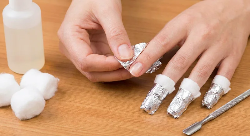 Palce owinięte wacikami i folią aluminiową podczas usuwania lakieru hybrydowego acetonem.