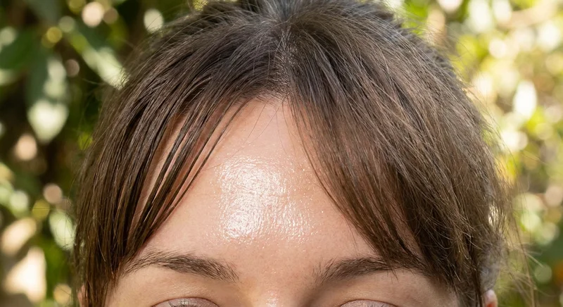 Zbliżenie na błyszczące od sebum czoło i zbijające się w pasma, tłuste włosy grzywki.